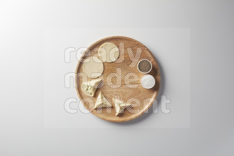 two closed sambosas and one open sambosa filled with cheese while salt, and black pepper aside in a wooden dish on a white background