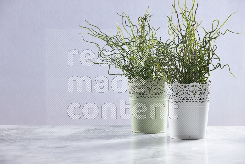 Two different artificial plants in white and green decorative pots on grey marble background