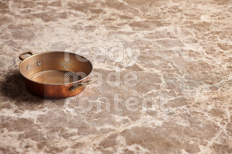 A small copper pan on beige marble background