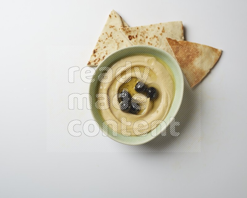 Hummus in a green plate garnished with black olives on a white background
