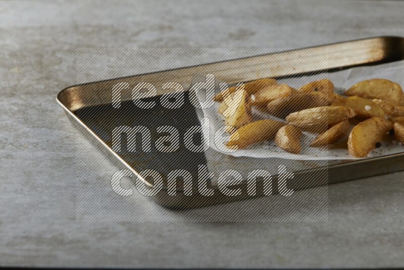 wedges potato on parchment paper in a black stainless steel rectangle tray on grey textured counter top