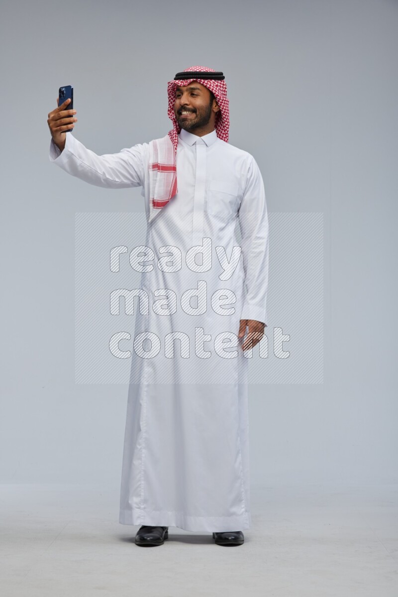 Saudi man Wearing Thob and shomag standing taking selfie on Gray background