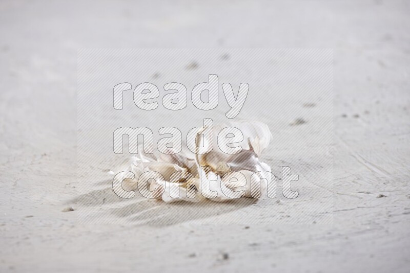 A cracked garlic bulb showing the cloves inside it on a white flooring
