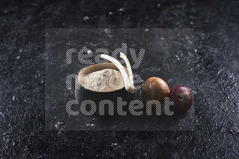 A black pottery bowl full of onion powder on black background