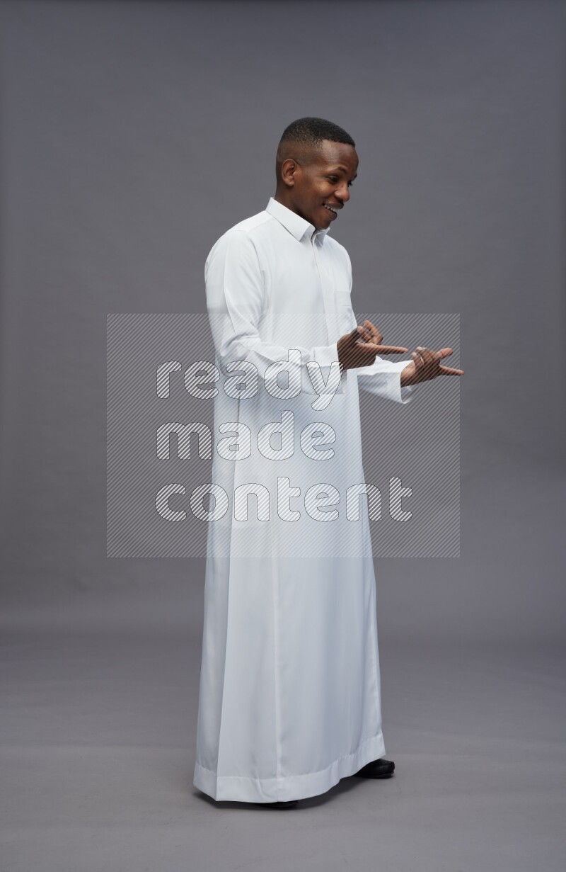 Saudi man wearing thob standing interacting with the camera on gray background