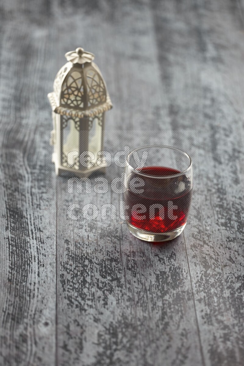 A white lantern with different drinks, dates, nuts, prayer beads and quran on grey wooden background