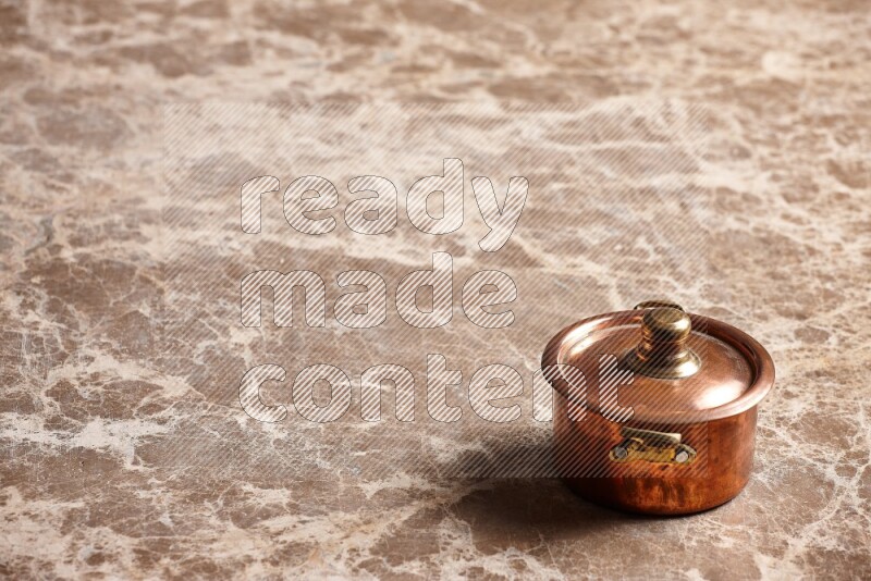 A small copper pot on beige marble background