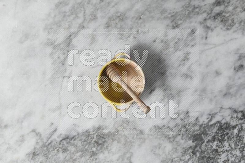 Multicolored pottery bowl with wooden honey dipper in it on grey marble background