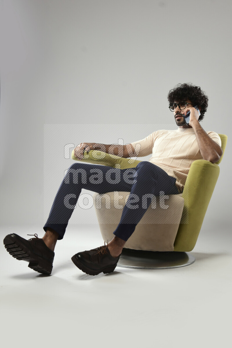 A man wearing casual sitting on a chair talking on the phone on white background