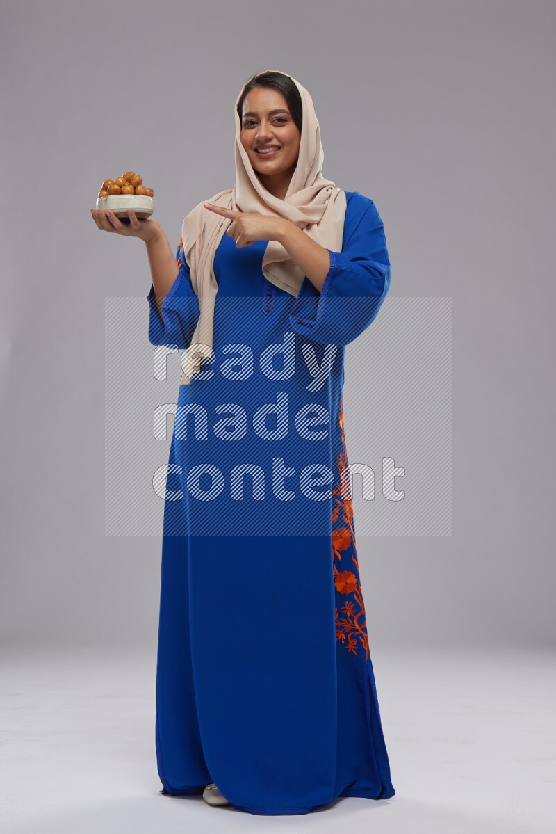 A Saudi woman standing wearing Jalabeya holding a plate of luqaimat