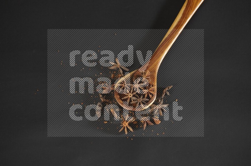Star Anise in a wooden spoon ladle with more anise on black flooring