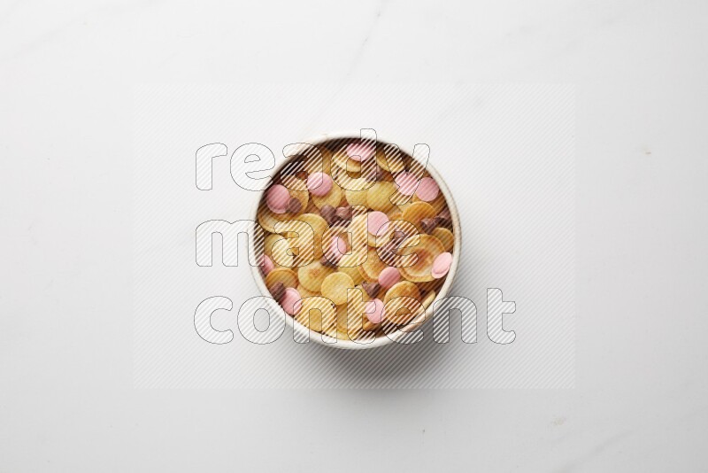 Top-view shot of mixed chocolate chips cereal pancakes in a round bowl on white background