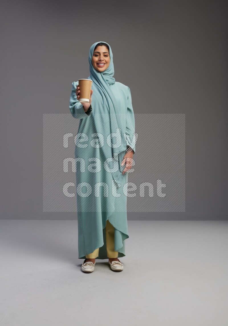 Saudi Woman wearing Abaya standing  holding paper cup on Gray background