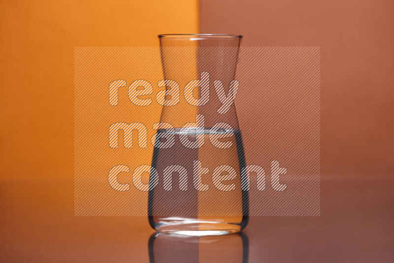 The image features a clear glassware filled with water, set against orange and dark orange background