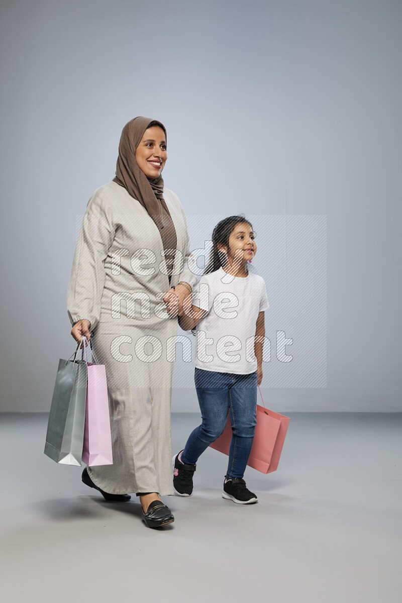Mom and daughter holding shopping bags on gray background
