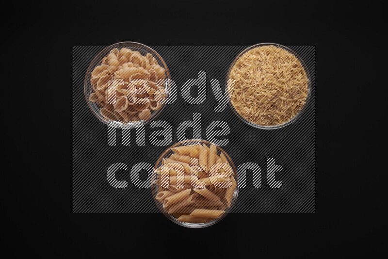 Different pasta types in glass bowls on black background