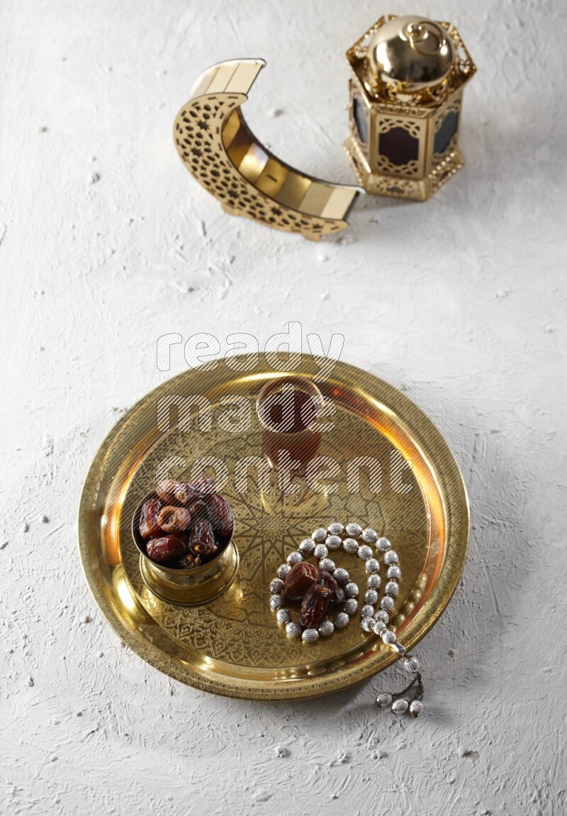 Dates in a metal bowl with tea and prayer beads on a tray beside lanterns in a light setup