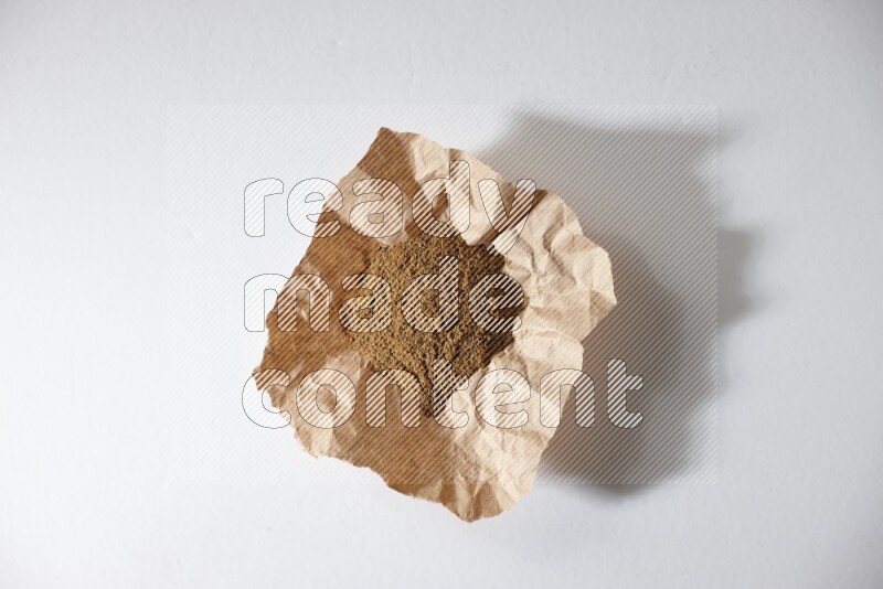 Cumin powder in a crumpled piece of paper on white flooring