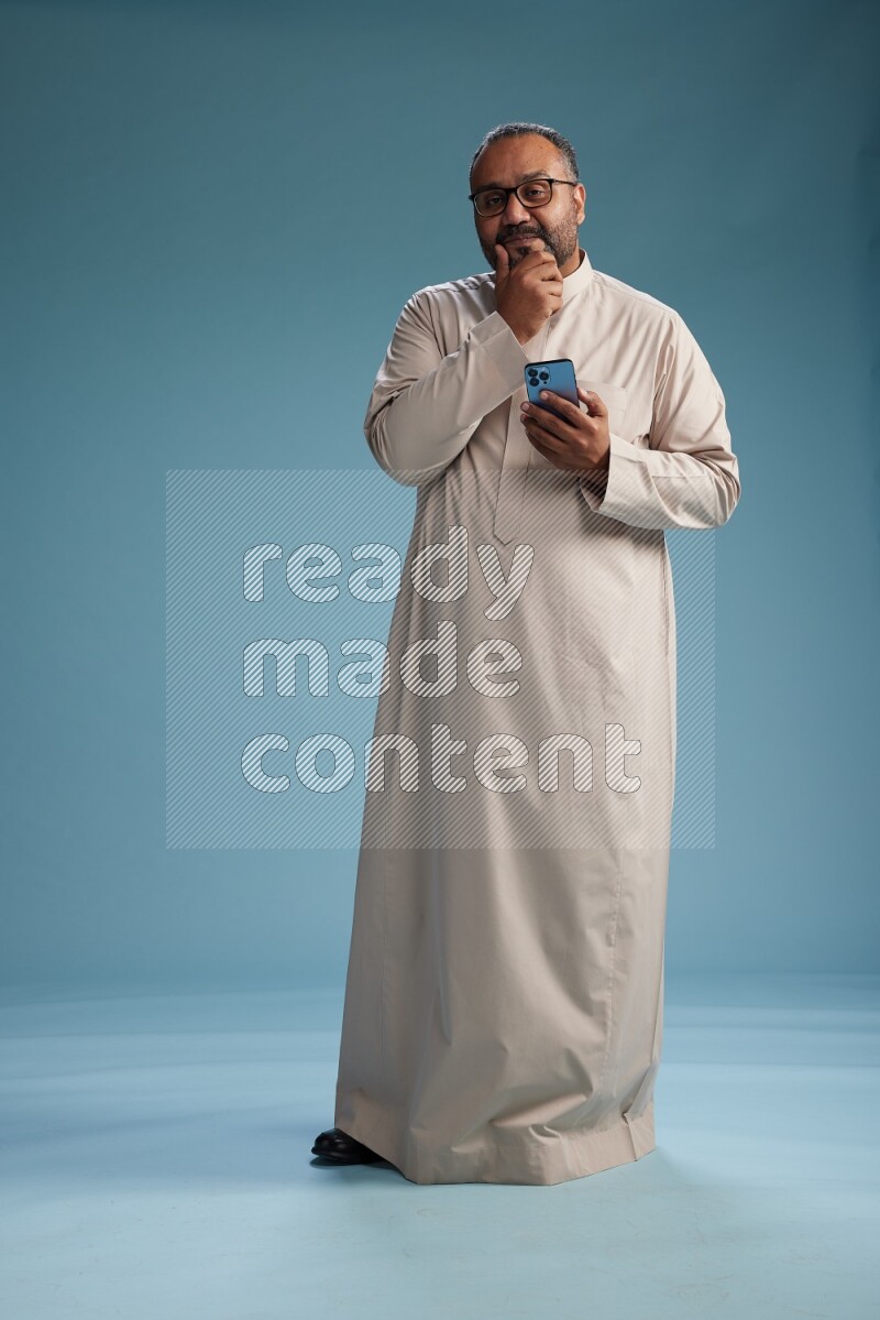 Saudi Man without shimag Standing texting on phone on blue background