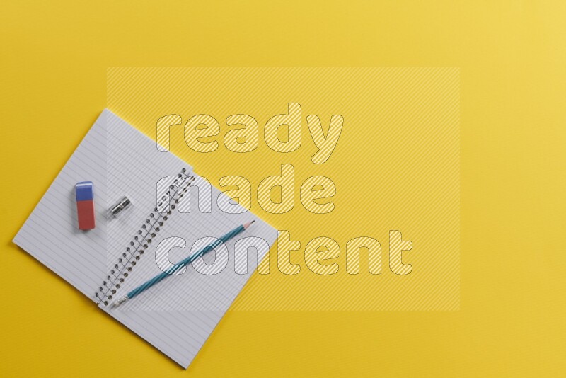 An open notebook with different school supplies on yellow background