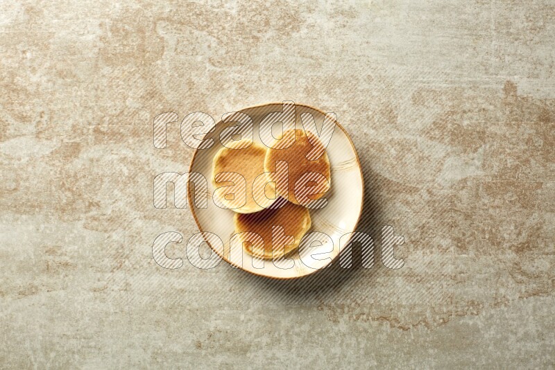 Three stacked plain mini pancakes in an irregular plate on beige background