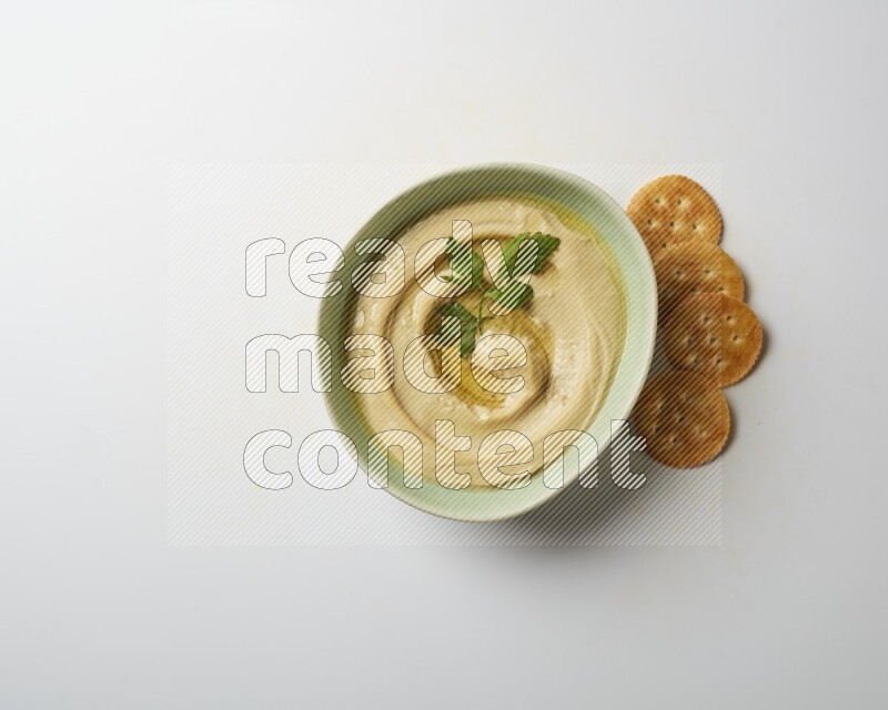 Hummus in a green plate garnished with parsley on a white background