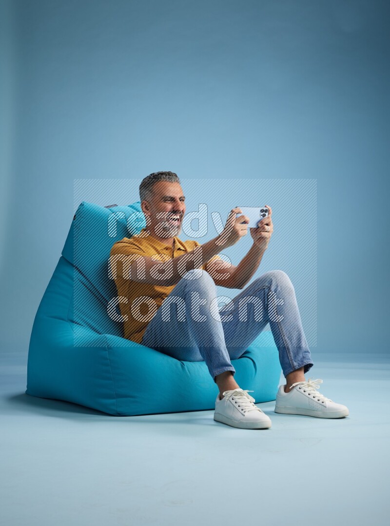A man sitting on a blue beanbag and playing on phone