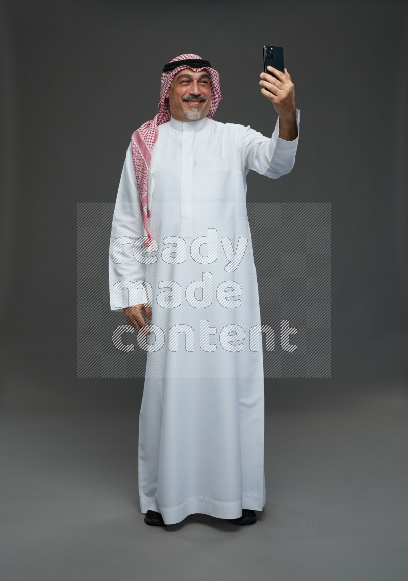 Saudi man with shomag Standing taking selfie on gray background