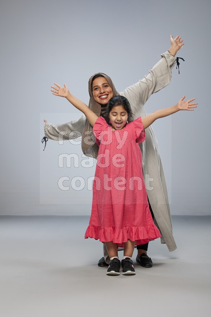 A girl and her mother interacting with the camera on gray background