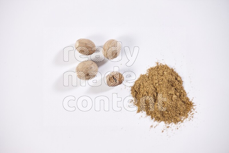 Nutmeg whole seeds with nutmeg powder beside it on a white flooring