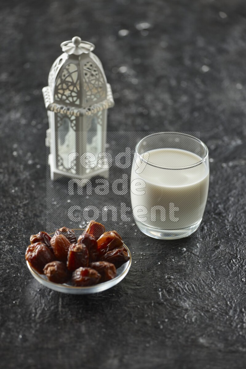 A white lantern with different drinks, dates, nuts, prayer beads and quran on textured black background