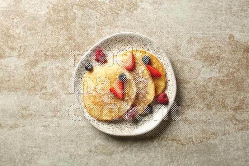 Three stacked mixed berries pancakes in an irregular plate on beige background