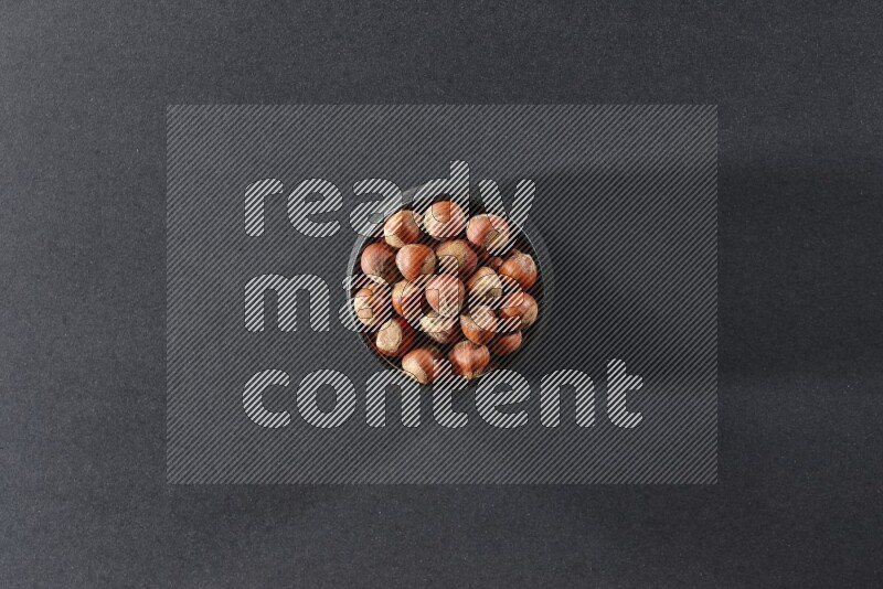 A black pottery bowl full of hazelnuts on a black background in different angles