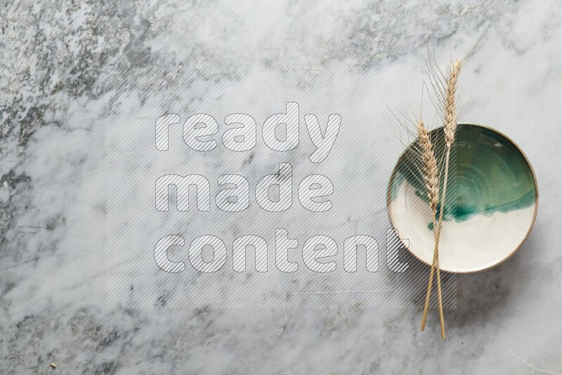 Wheat stalks on multicolored pottery plate on grey marble background