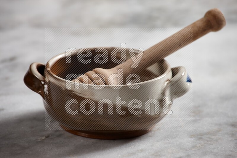 Multicolored pottery bowl with wooden honey dipper in it on grey marble background