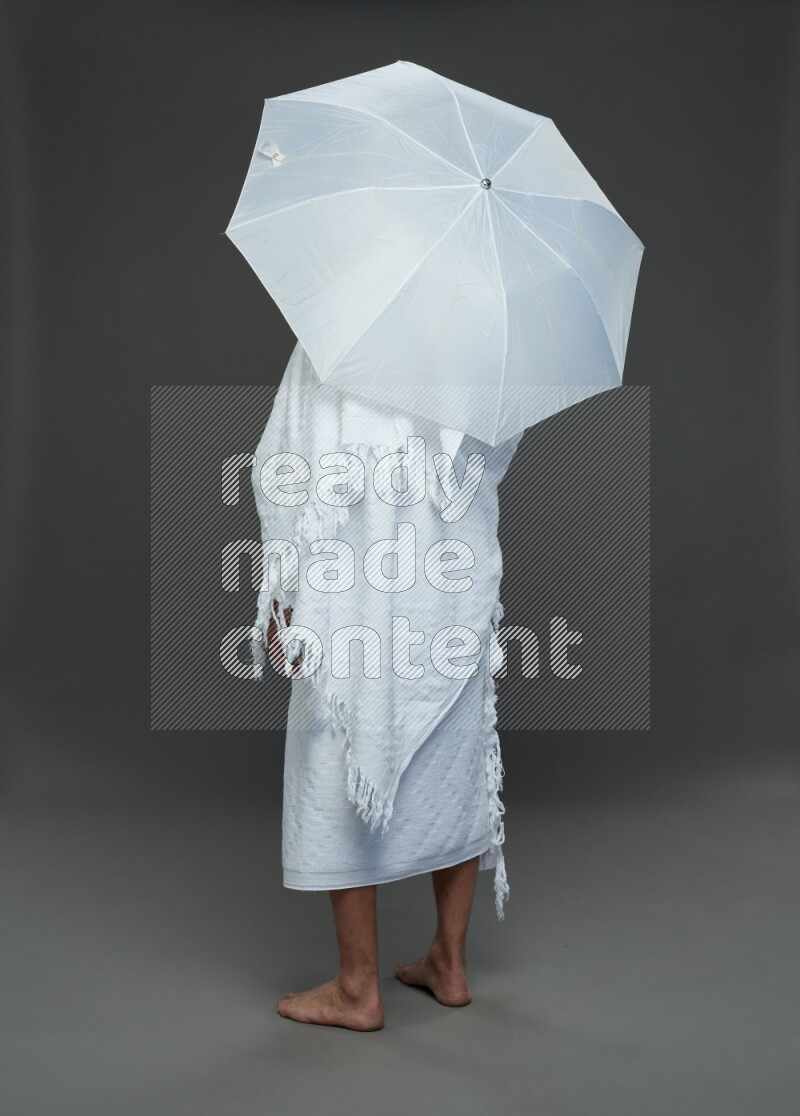 A man wearing Ehram Standing holding umbrella on gray background