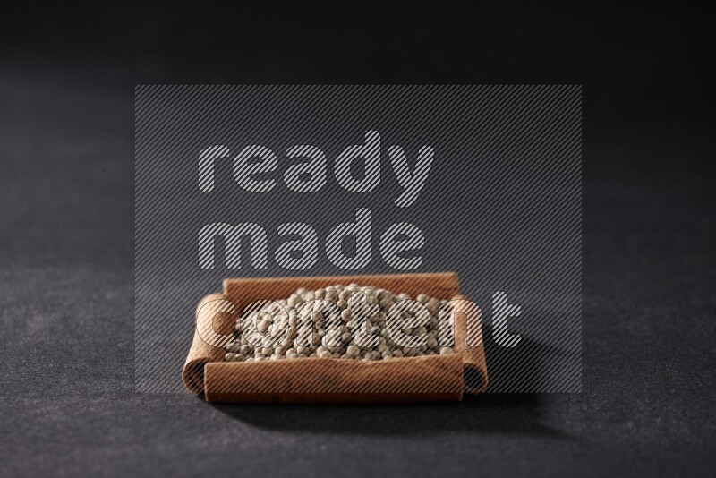 A single square of cinnamon sticks full of white pepper on black flooring