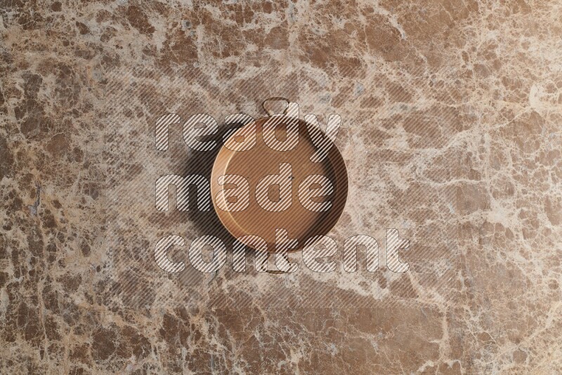 A small copper pan on beige marble background