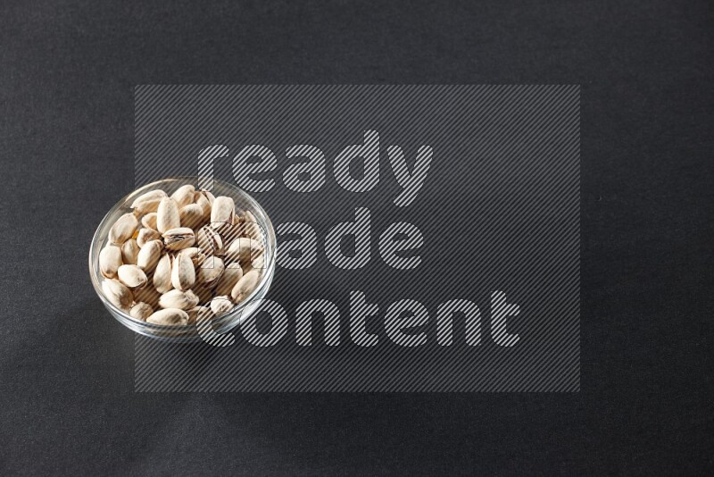 A glass bowl full of pistachios on a black background in different angles