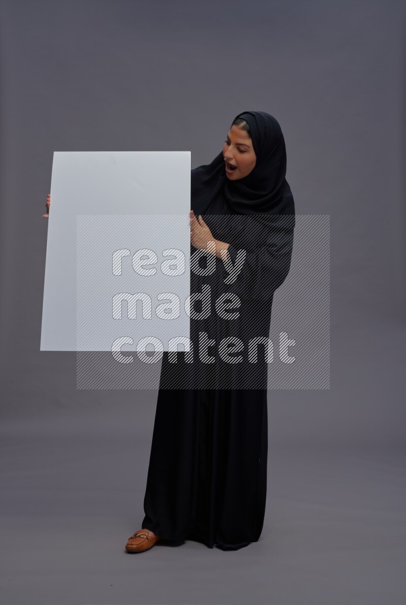 Saudi woman wearing Abaya standing holding white board on gray background