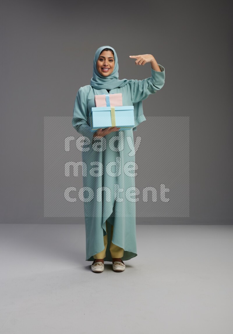 Saudi Woman wearing Abaya standing holding gift box on Gray background
