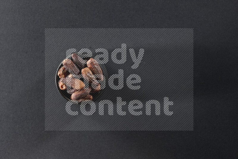 A black pottery bowl full of dried dates on a black background in different angles