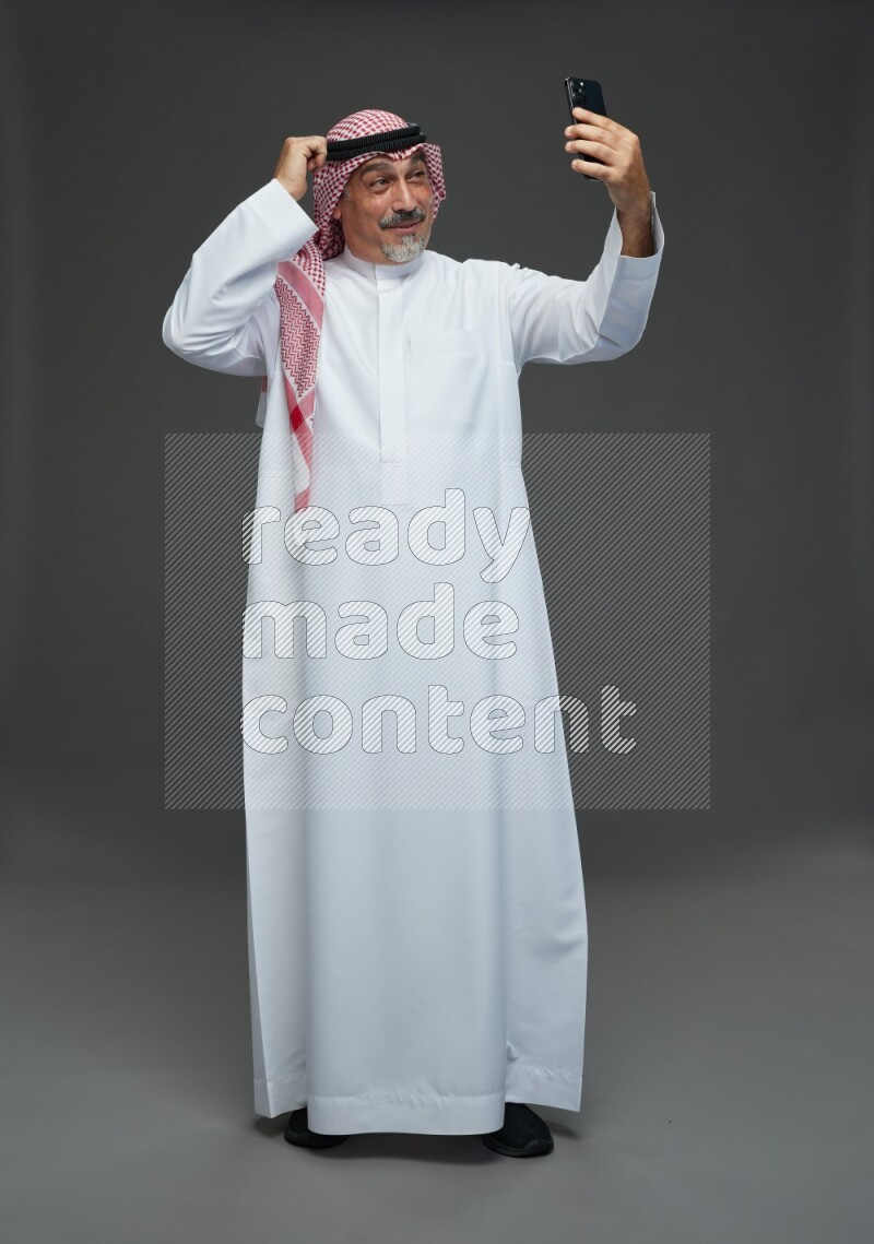 Saudi man with shomag Standing taking selfie on gray background