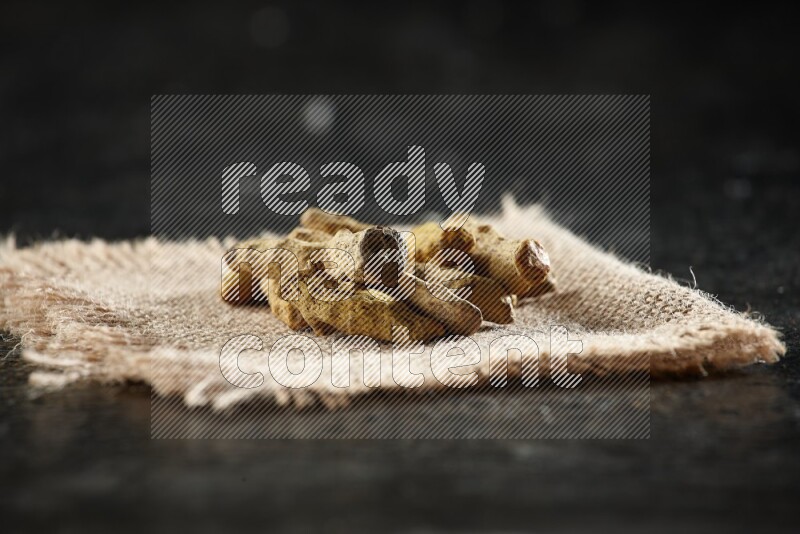 Dried turmeric whole fingers on a burlap piece of fabric on textured black flooring