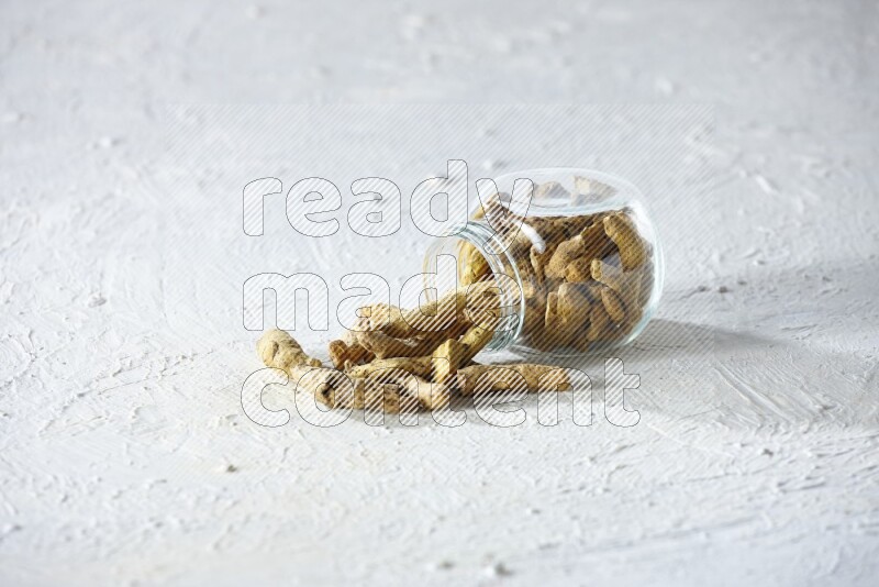 A flipped glass spice jar full of dried turmeric fingers and fell out it on textured white flooring