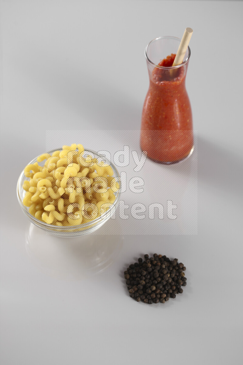 معكرونة مع صلصة طماطم مع مكونات متنوعة من الطماطم والثوم والريحان والفلفل الأحمر والفلفل الأسود والفلفل الأبيض وأوراق الغار والهيل وسنابل القمح على خلفية رمادية