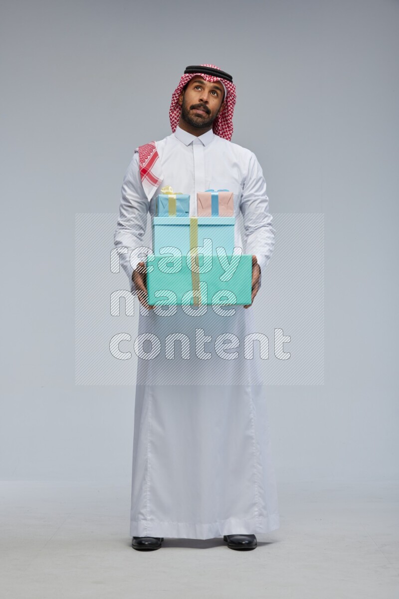 Saudi man Wearing Thob and shomag standing holding gift box on Gray background
