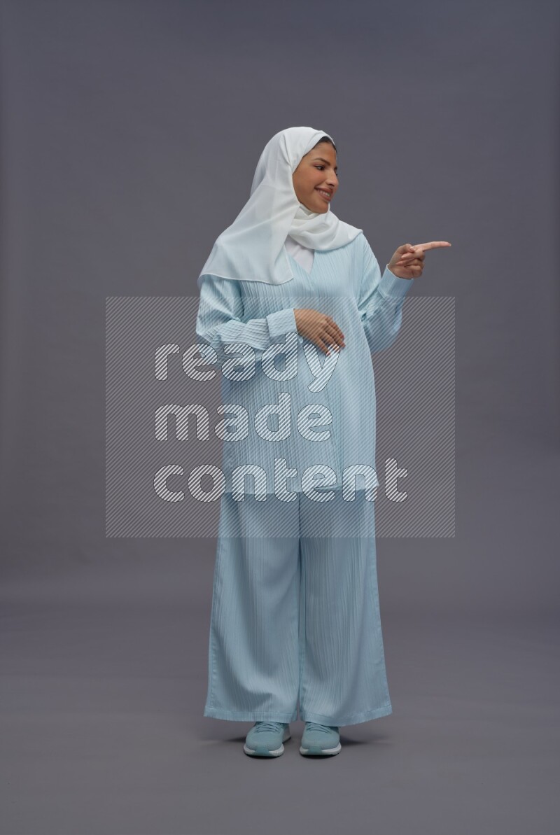 Saudi woman wearing hijab clothes standing interacting with the camera on gray background