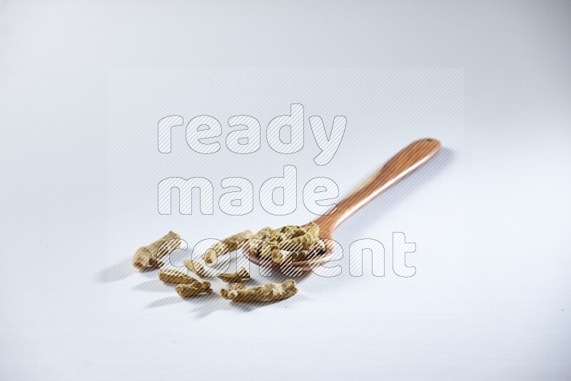 مغرفة خشبية مليئة بأصابع الكركم المجففة على خلفية بيضاء