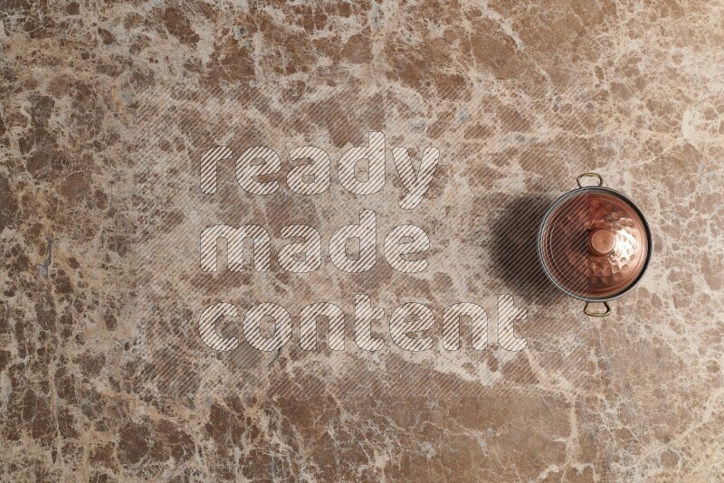 A small copper pot on beige marble background